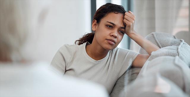 Woman sitting on a couch looking stressed and forlorn like she can't escape the trap that is her mind (it's also giving a little sad beige children)