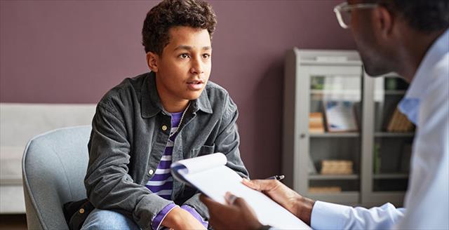 A young teen with an open and honest face sits speaking to a psychologist across from him