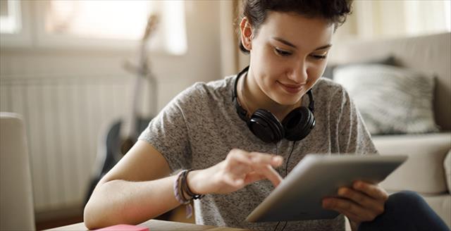 Young woman seated at desk interacting with content on a tablet