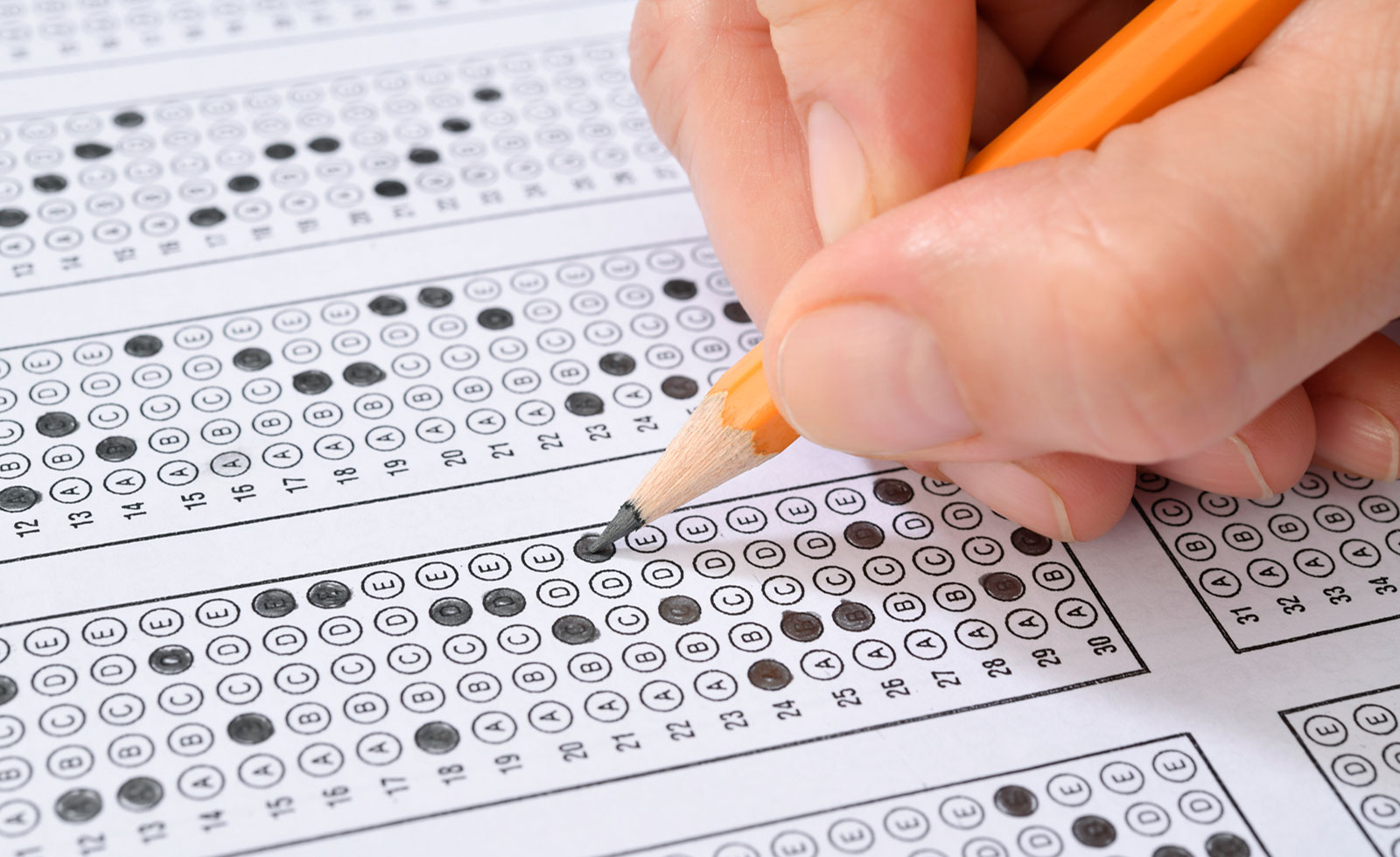 Hand holding pencil fills in scantron exam sheet.
