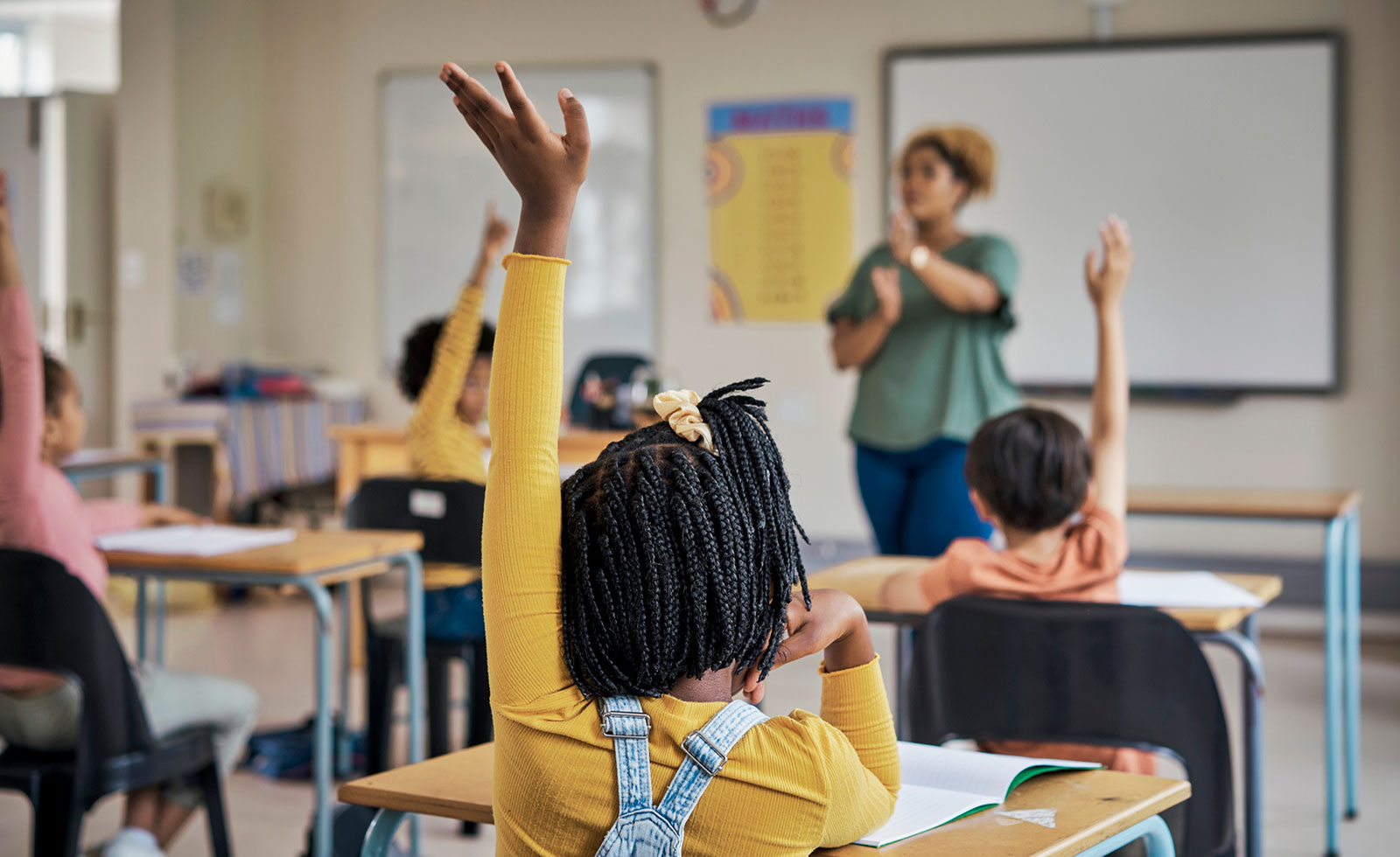Teacher in classroom with kids’ hands raised to answer question.