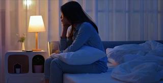 A woman sitting up in bed at night, likely experiencing insomnia or sleep